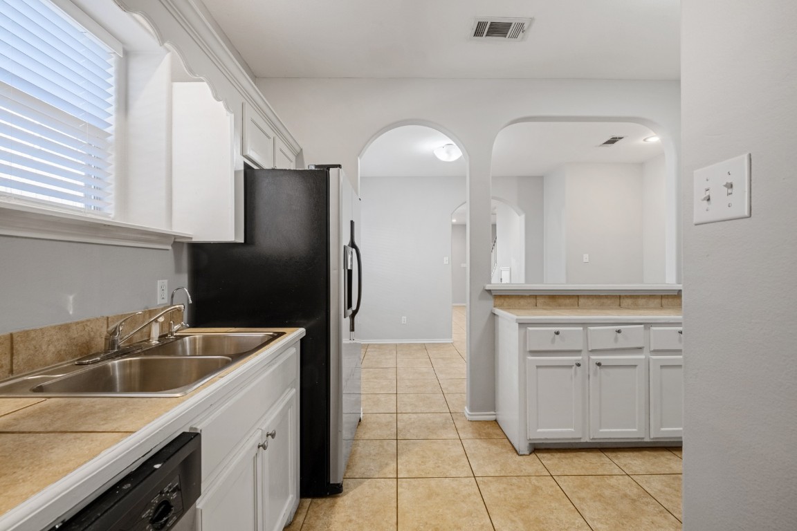Kitchen featuring white cabinetry, light tile patterned flooring, dishwashing machine, stainless steel fridge with ice dispenser, and tile countertops