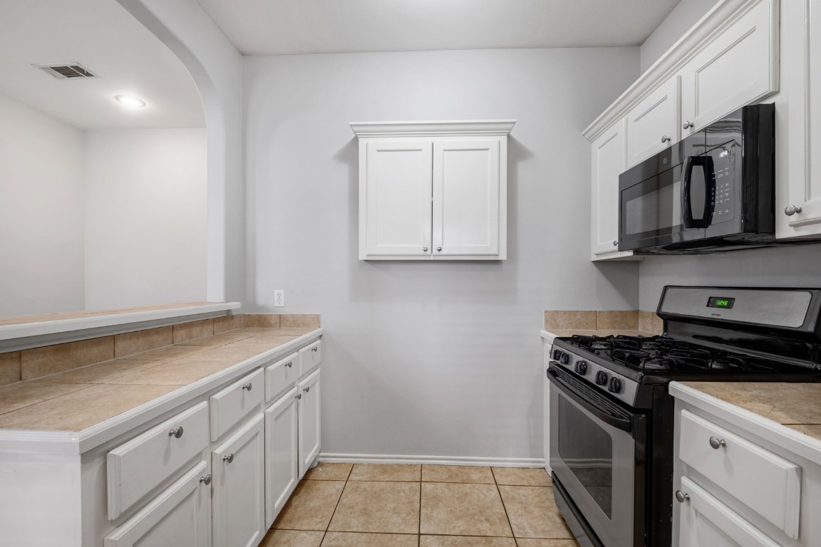 2906 Pearl Street, Unit C Austin, TX 78705 - Photo 8 of 25 Kitchen featuring gas stove, white cabinets, black microwave, light tile patterned flooring, and arched walkways