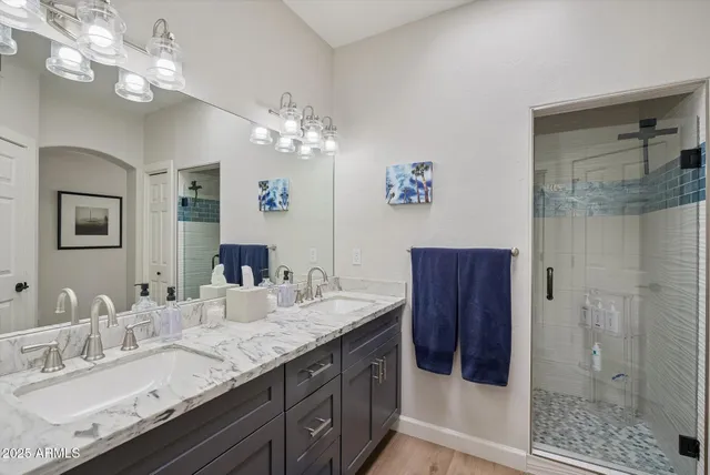 a bathroom with a granite countertop double vanity sink a mirror and shower