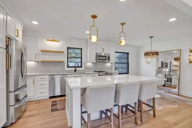 a kitchen with stainless steel appliances granite countertop a sink a stove a refrigerator cabinets and chairs