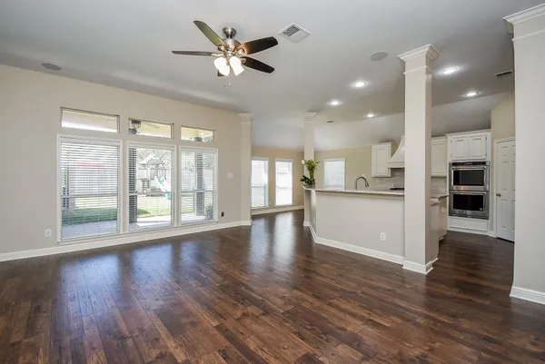 a view of an empty room with wooden floor and a kitchen