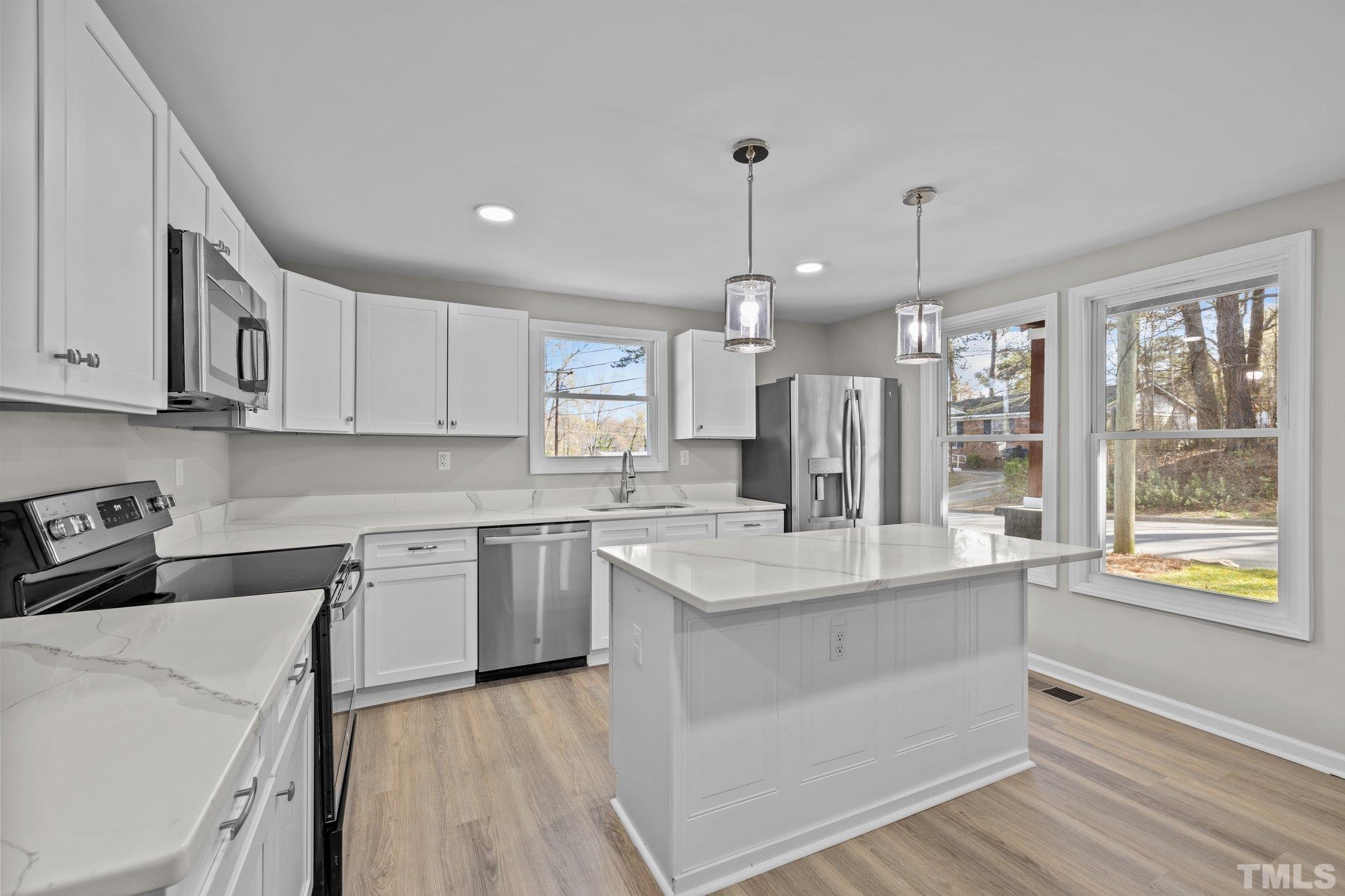 2908 Woods Place Raleigh, NC 27607 - Photo 25 of 38 a large white kitchen with kitchen island granite countertop a stove a sink a refrigerator and white cabinets with wooden floor