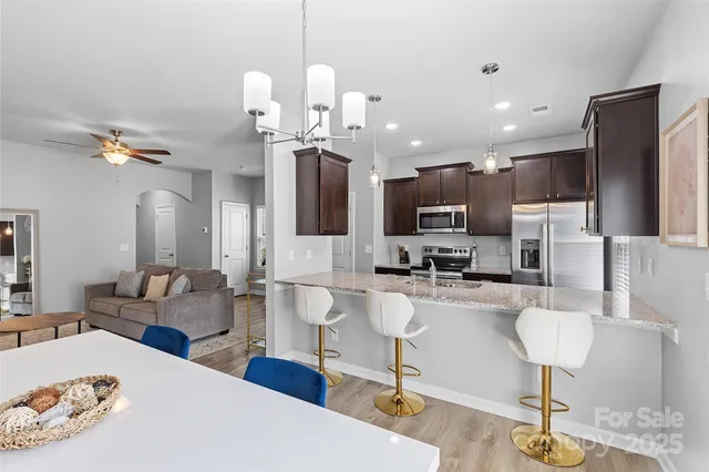 a kitchen with stainless steel appliances kitchen island granite countertop a refrigerator a stove a oven a sink with a dining table and chairs with wooden floor