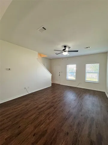 a view of an empty room with wooden floor and ceiling fan