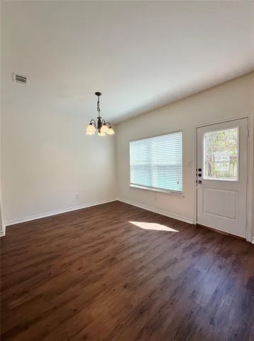 an empty room with wooden floor chandelier and windows