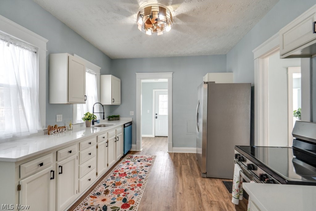 12 South 4th Street Rittman, OH 44270 - Photo 14 of 48 Kitchen featuring stainless steel appliances, white cabinets, a textured ceiling, light wood finished floors, and healthy amount of natural light