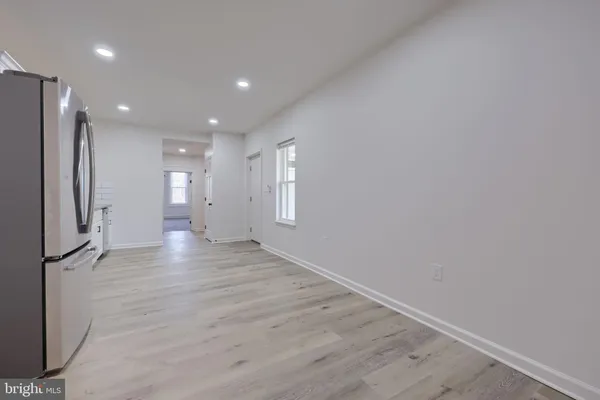 a view of an empty room with wooden floor and a kitchen