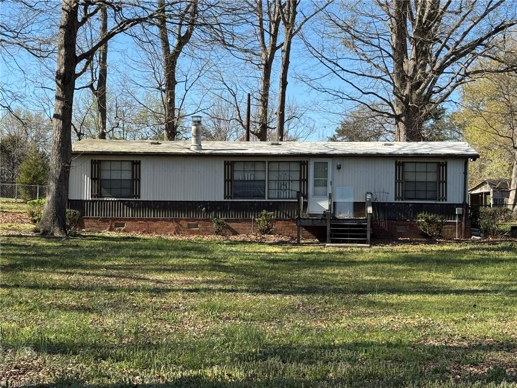 2023 Benaja Road Reidsville, NC 27320 - Photo 1 of 36 Front Exterior with Wooden Steps and Sidewalk at 2023 Benaja Road, Reidsville, NC 27320, Rockingham County. Angled view showing the wooden front steps and concrete sidewalk approach. Brick skirting and white siding with dark shutters. Large mature trees frame the property.