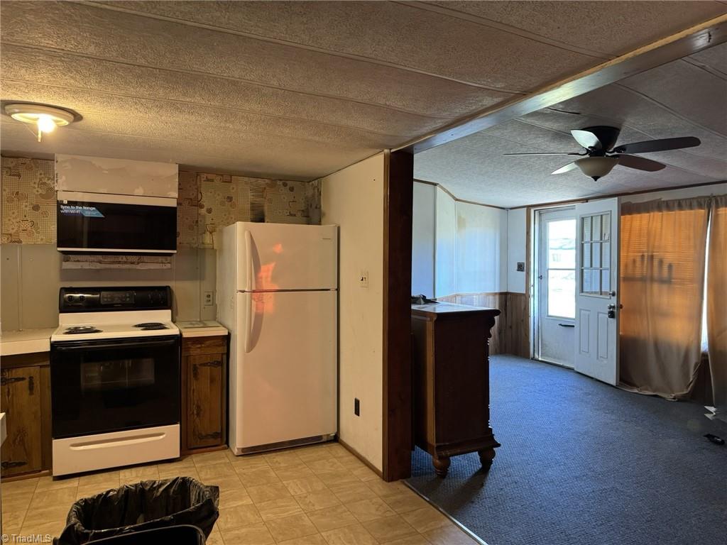 2023 Benaja Road Reidsville, NC 27320 - Photo 13 of 36 Kitchen Open to Living Room with Appliances at 2023 Benaja Road, Reidsville, NC 27320, Rockingham County. Kitchen with electric range, white refrigerator, and overhead microwave. Wood cabinets with tile flooring. Open view to the living room. Peninsula counter separates spaces.