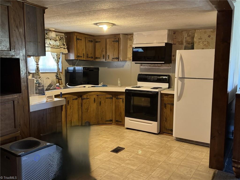 2023 Benaja Road Reidsville, NC 27320 - Photo 15 of 36 Kitchen with Peninsula Counter and Full Appliance View at 2023 Benaja Road, Reidsville, NC 27320, Rockingham County. Wide view of the kitchen showing peninsula counter, curved cabinetry, electric range, microwave, and white refrigerator. Tile flooring and decorative hardware.