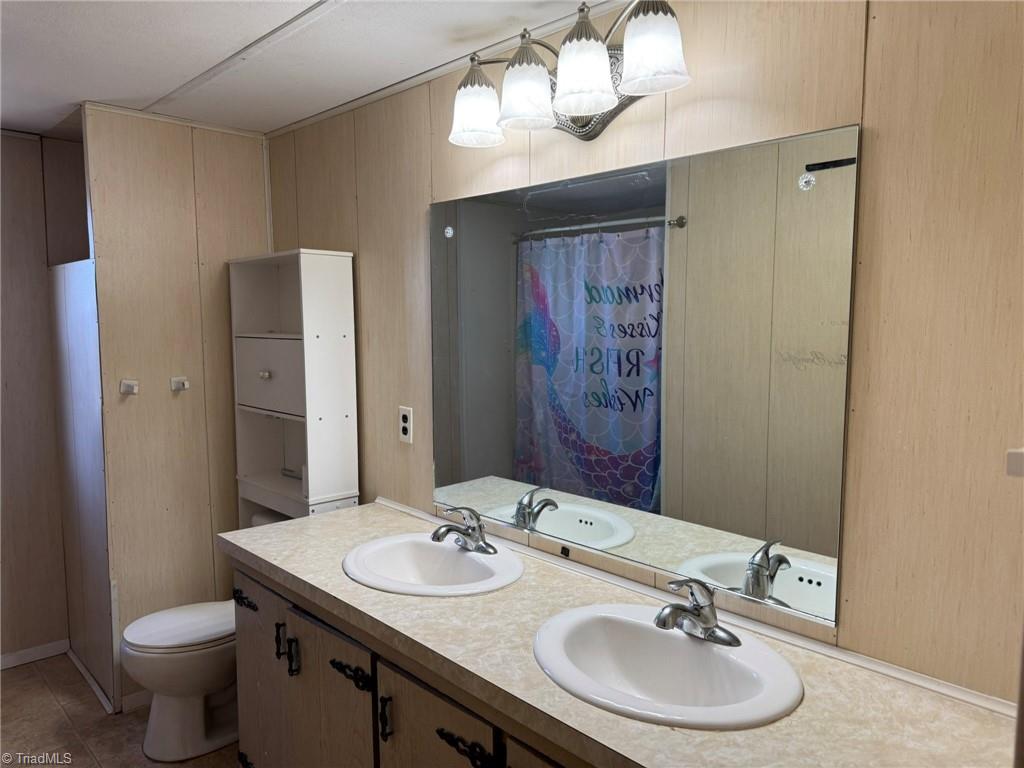 2023 Benaja Road Reidsville, NC 27320 - Photo 17 of 36 Primary Bathroom with Double Vanity and Large Mirror at 2023 Benaja Road, Reidsville, NC 27320, Rockingham County. Primary bathroom featuring a double vanity with dual sinks and large wall-mounted mirror. Three-light fixture above. Toilet and storage cabinet. Tile flooring.