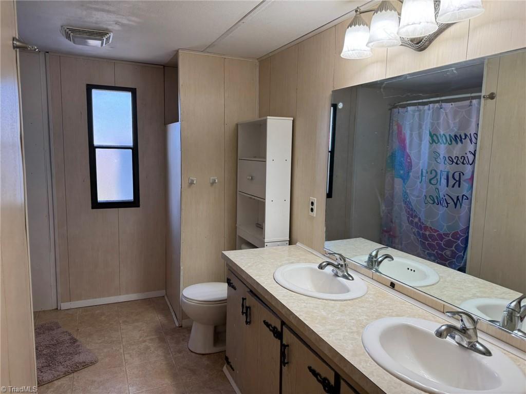 2023 Benaja Road Reidsville, NC 27320 - Photo 18 of 36 Primary Bathroom with Double Vanity and Storage Cabinet at 2023 Benaja Road, Reidsville, NC 27320, Rockingham County. Wider view of the primary bathroom showing double vanity, frosted window, and tall storage cabinet. Tile flooring. Three-light vanity fixture and large mirror.