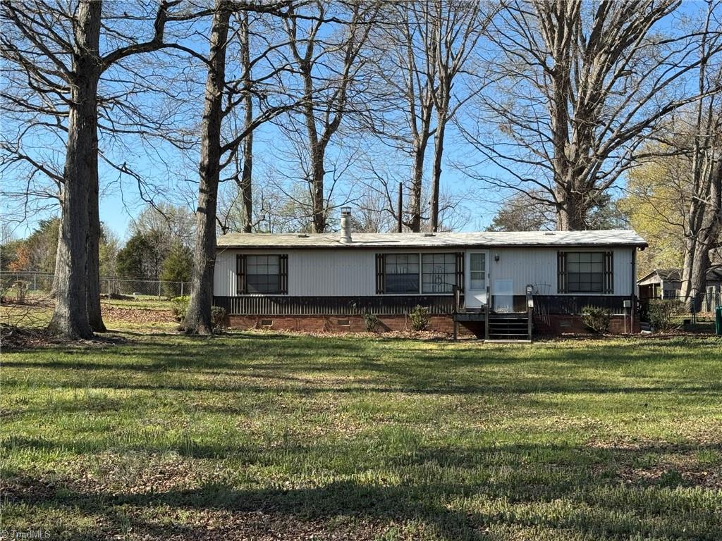 2023 Benaja Road Reidsville, NC 27320 - Photo 2 of 36 Front Exterior with Wooden Steps and Sidewalk at 2023 Benaja Road, Reidsville, NC 27320, Rockingham County. Angled view showing the wooden front steps and concrete sidewalk approach. Brick skirting and white siding with dark shutters. Large mature trees frame the property.