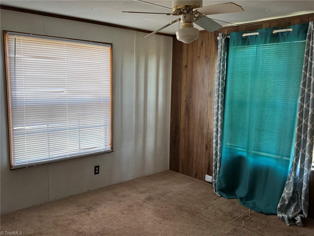 2023 Benaja Road Reidsville, NC 27320 - Photo 20 of 36 Bedroom Two with Ceiling Fan and Teal Curtains at 2023 Benaja Road, Reidsville, NC 27320, Rockingham County. Second bedroom with carpeted flooring and ceiling fan. Window with blinds and teal curtains. Wood paneling accent wall. Comfortable room for furnishing.