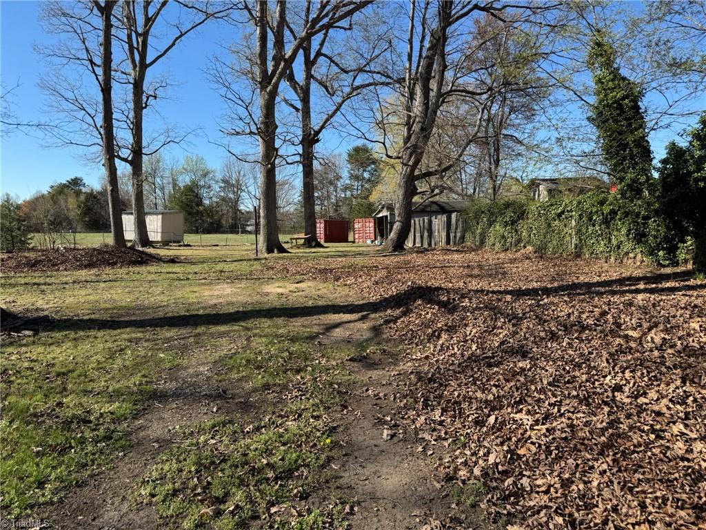 2023 Benaja Road Reidsville, NC 27320 - Photo 26 of 36 Backyard with Outbuildings and Mature Trees at 2023 Benaja Road, Reidsville, NC 27320, Rockingham County. Backyard view showing outbuildings including storage containers and a wooden shed. Mature hardwood trees throughout. Spacious lot with room for outdoor projects.