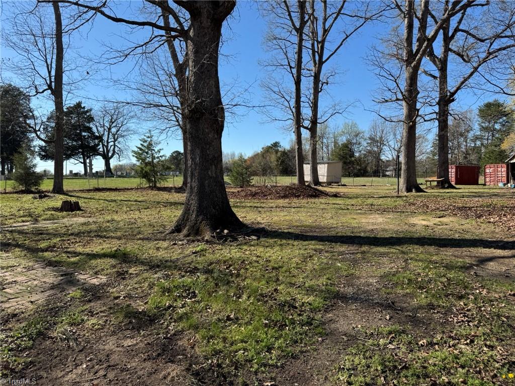 2023 Benaja Road Reidsville, NC 27320 - Photo 27 of 36 Backyard Wide View with Mature Hardwood Trees at 2023 Benaja Road, Reidsville, NC 27320, Rockingham County. Wide view of the backyard with mature hardwood trees and open grass. Storage buildings and containers in the background. Level terrain with usable space.