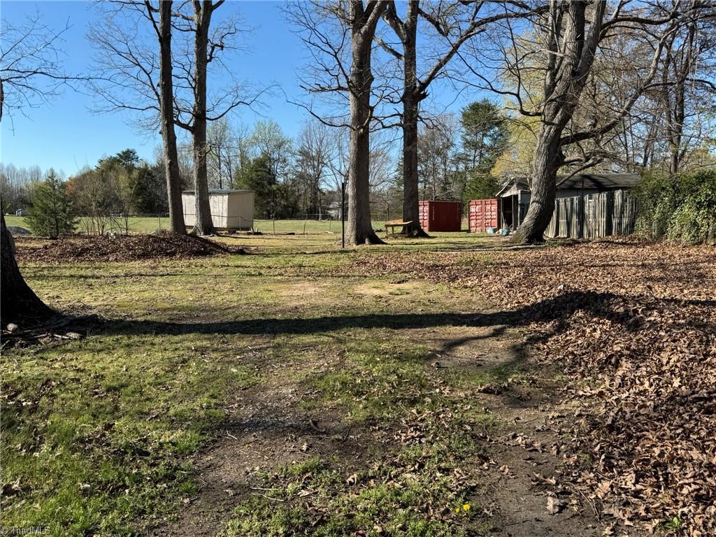 2023 Benaja Road Reidsville, NC 27320 - Photo 29 of 36 Backyard Wide Angle with Storage Containers at 2023 Benaja Road, Reidsville, NC 27320, Rockingham County. Wide-angle backyard view with storage containers, outbuildings, and mature hardwoods. Large open lot with a mix of grass and leaf ground cover.