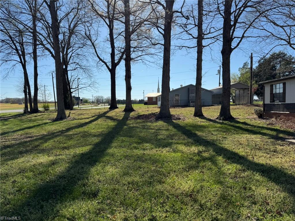 2023 Benaja Road Reidsville, NC 27320 - Photo 3 of 36 Side Yard with Mature Trees and Church Steeple View at 2023 Benaja Road, Reidsville, NC 27320, Rockingham County. Side yard looking toward the road with mature hardwood trees lining the property. Church steeple visible in the distance. Spacious green lawn with rural feel.