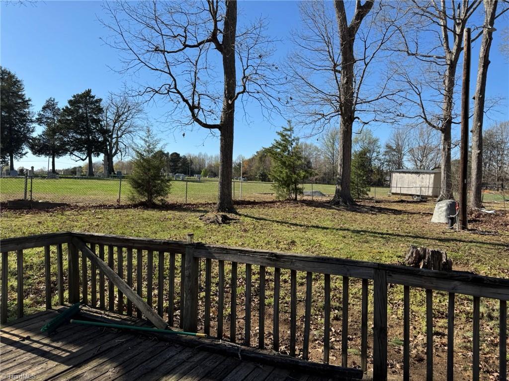 2023 Benaja Road Reidsville, NC 27320 - Photo 30 of 36 Backyard Wide Angle with Storage Containers at 2023 Benaja Road, Reidsville, NC 27320, Rockingham County. Wide-angle backyard view with storage containers, outbuildings, and mature hardwoods. Large open lot with a mix of grass and leaf ground cover.
