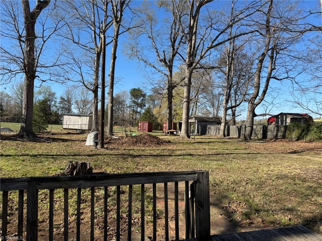 2023 Benaja Road Reidsville, NC 27320 - Photo 31 of 36 Deck View of Backyard with Outbuildings at 2023 Benaja Road, Reidsville, NC 27320, Rockingham County. View from the deck at the backyard with outbuildings and storage containers. Mature hardwood trees frame the property. Brick walkway visible below.
