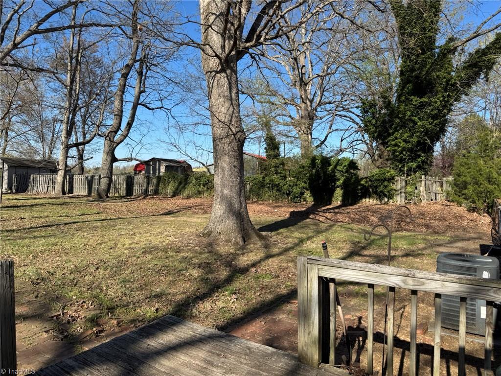2023 Benaja Road Reidsville, NC 27320 - Photo 32 of 36 Side Yard from Deck with Fenced Area and HVAC at 2023 Benaja Road, Reidsville, NC 27320, Rockingham County. View from the deck of the side yard showing fenced area, HVAC unit, and mature trees. Ivy-covered hedgerow along the property boundary.