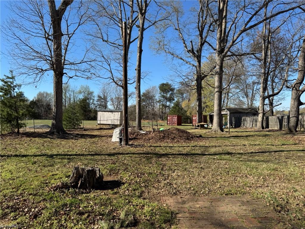 2023 Benaja Road Reidsville, NC 27320 - Photo 34 of 36 Backyard with Brick Walkway and Outbuildings at 2023 Benaja Road, Reidsville, NC 27320, Rockingham County. Backyard showing a brick walkway, utility pole, and multiple outbuildings including a storage shed and containers. Mature trees and chain-link fencing.