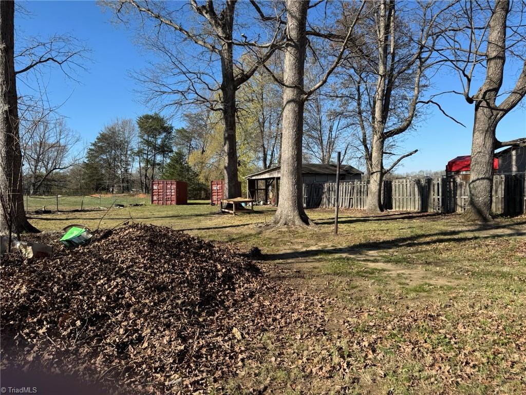 2023 Benaja Road Reidsville, NC 27320 - Photo 35 of 36 Backyard with Storage Containers and Covered Shed at 2023 Benaja Road, Reidsville, NC 27320, Rockingham County. Backyard view showing storage containers, covered shed, and fencing. Large leaf pile in the foreground. Mature hardwood trees throughout the spacious lot.