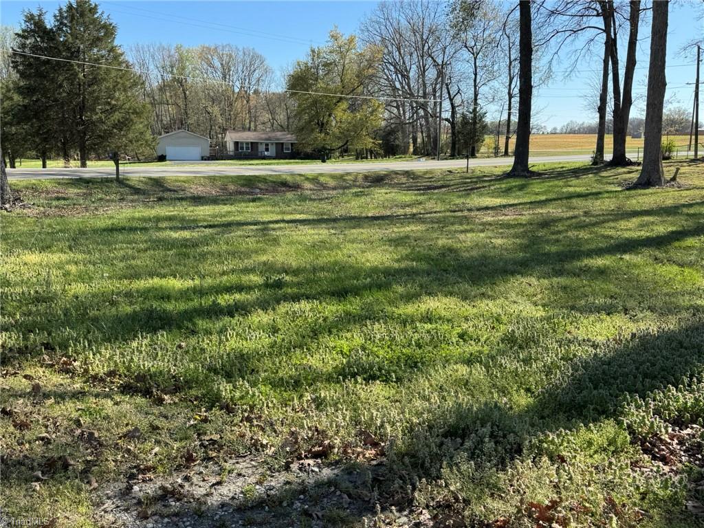 2023 Benaja Road Reidsville, NC 27320 - Photo 5 of 36 Front Yard with Road Frontage and Farmland Views at 2023 Benaja Road, Reidsville, NC 27320, Rockingham County. Front yard showing road frontage with open farmland across the road. Mature hardwood trees line the property. Neighboring home visible. Rural Rockingham County setting.