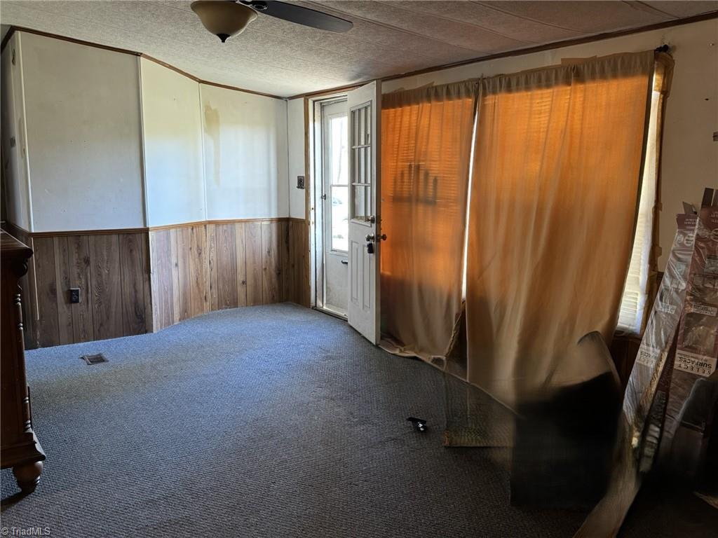 2023 Benaja Road Reidsville, NC 27320 - Photo 7 of 36 Living Room with Entry Door and Wood Paneling at 2023 Benaja Road, Reidsville, NC 27320, Rockingham County. Living room with carpeted floors and wood paneling wainscoting. Front entry door with window provides natural light. Ceiling fan overhead for air circulation.