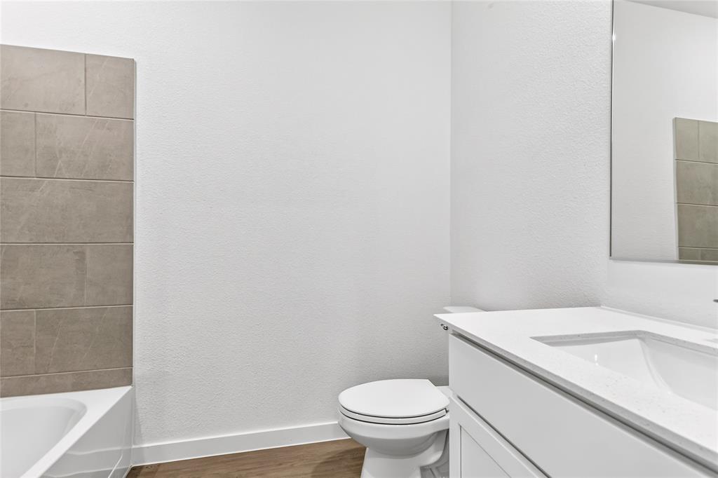 656 Waymaker Way Princeton, TX 75407 - Photo 17 of 40 Bathroom featuring a white vanity with integrated sink, a rectangular mirror, a white toilet, and a bathtub with large format tile surround