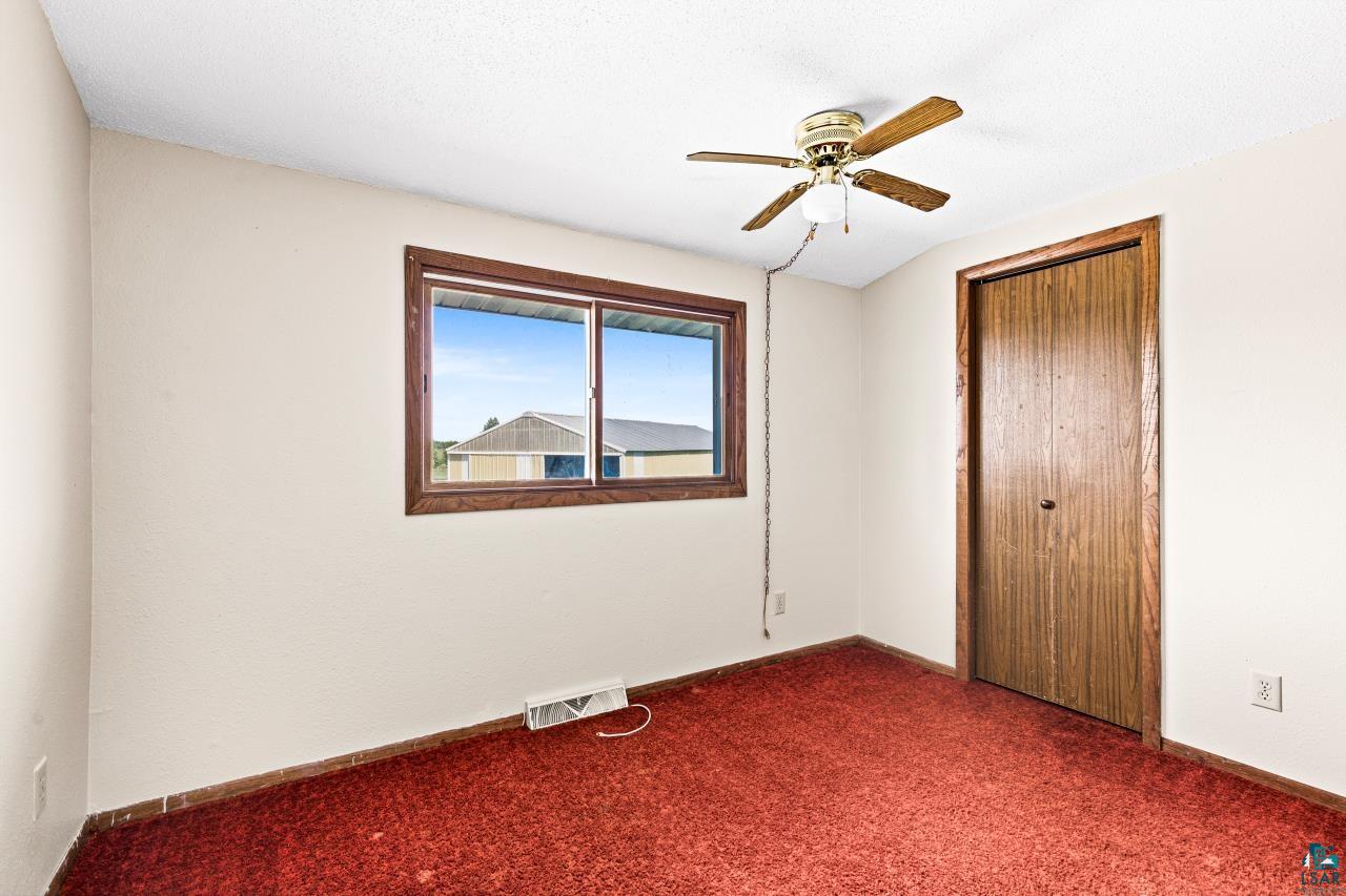 6606 Metso Road Kettle River, MN 55757 - Photo 24 of 84 Room featuring a window with wood-finish trim, a wood-finish bi-fold door, a ceiling fan with integrated lighting, and red carpeting