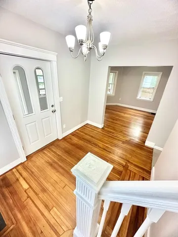 a view of an empty room with wooden floor and chandelier