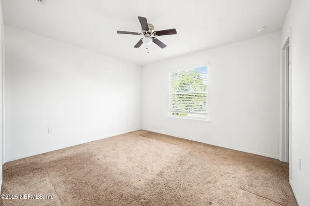an empty room with ceiling fan and windows