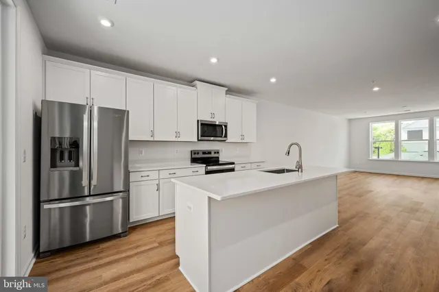 a kitchen with stainless steel appliances a refrigerator oven a sink and white cabinets with wooden floor