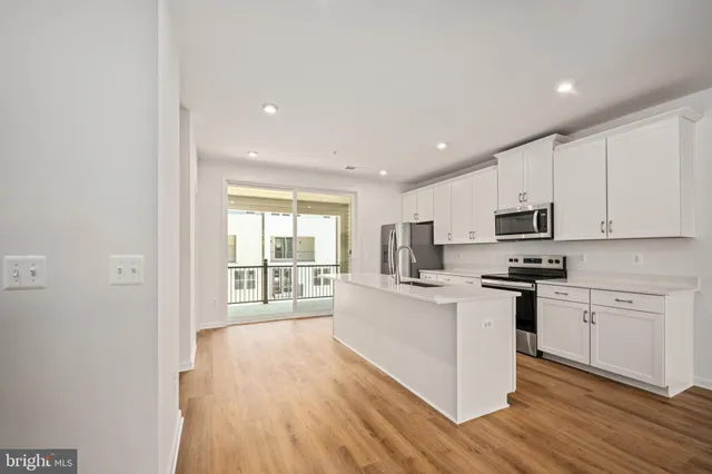 a kitchen with stainless steel appliances granite countertop a stove top oven a sink dishwasher and a refrigerator with wooden floor