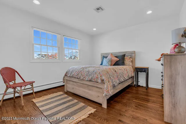 a bedroom with a bed a chair and potted plant on the wooden floor