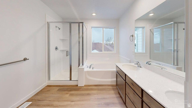 777 Pheasantbrook Drive, Unit 2B Centerville, UT 84014 - Photo 18 of 42 Contemporary bathroom featuring a dual vanity with light-colored countertops, a built-in tub, a separate glass-enclosed shower, and wood-finish flooring