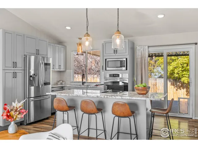 a kitchen with stainless steel appliances kitchen island granite countertop a dining table chairs and white cabinets