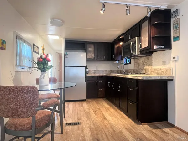 a kitchen with stainless steel appliances granite countertop a refrigerator a sink dishwasher a stove and a dining table with wooden floor