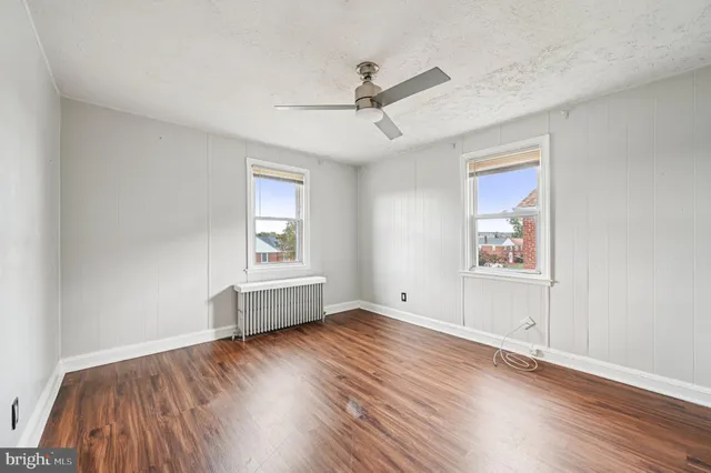 an empty room with wooden floor chandelier fan and windows