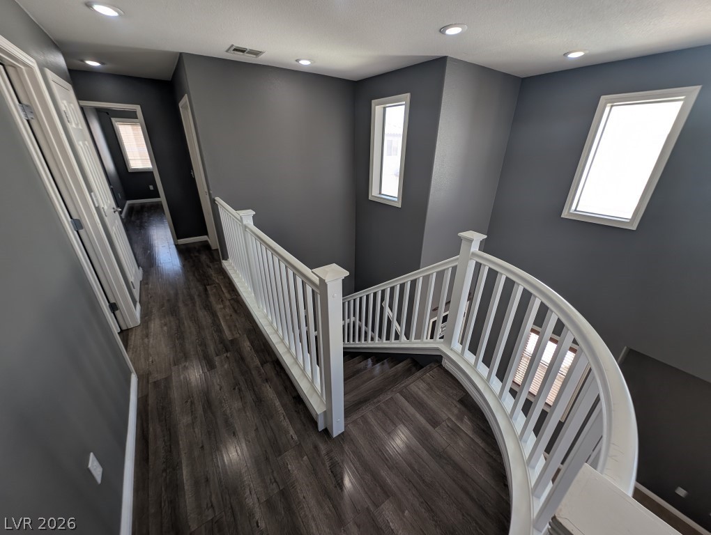 9121 Spoonbill Ridge Place Las Vegas, NV 89143 - Photo 17 of 26 Graceful curved staircase with pristine white railing, leading to an upper-level hallway with rich hardwood flooring.