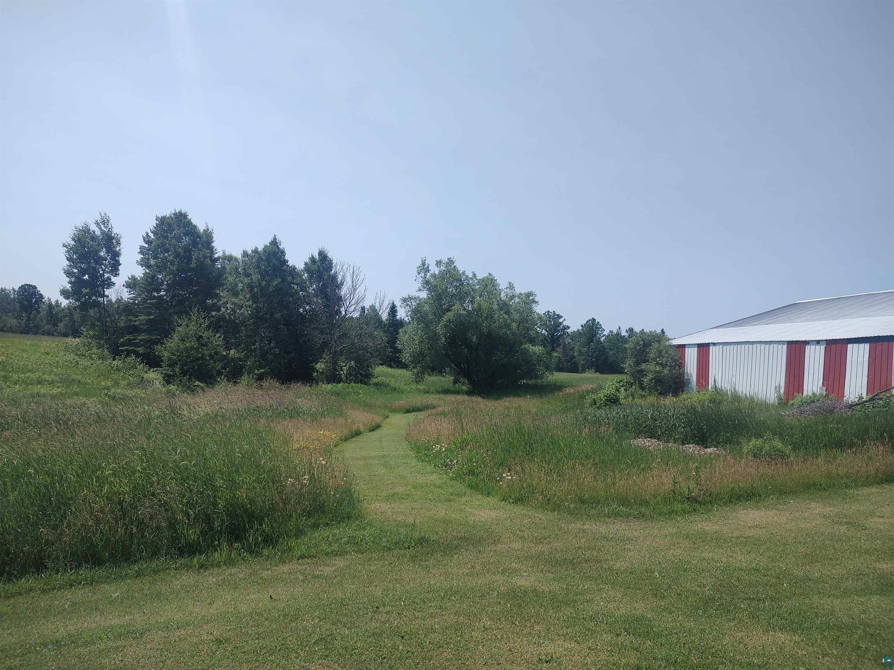2585 Hautala Road Iron River, WI 54847 - Photo 24 of 28 Expansive grassy landscape featuring a mown path, diverse mature trees, and a barn with red and white siding