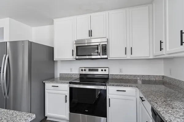 a kitchen with stainless steel appliances granite countertop a refrigerator stove and white cabinets