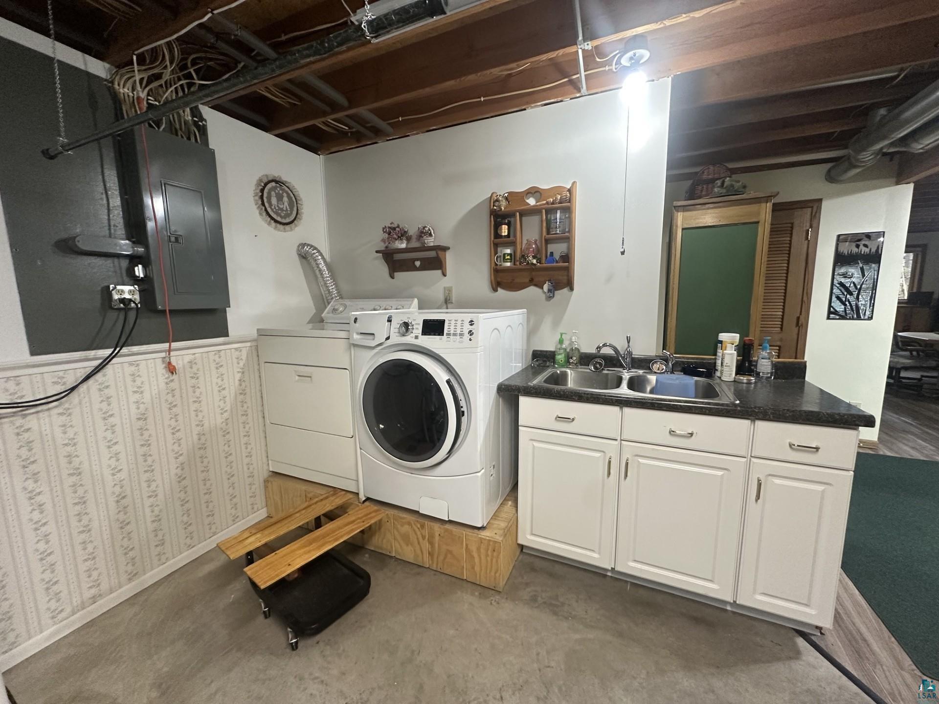 81 Hautaluoma Road Esko, MN 55733 - Photo 32 of 43 Utility area featuring a dual-basin stainless steel sink with white cabinetry, black countertop, exposed ceiling joists, and concrete flooring