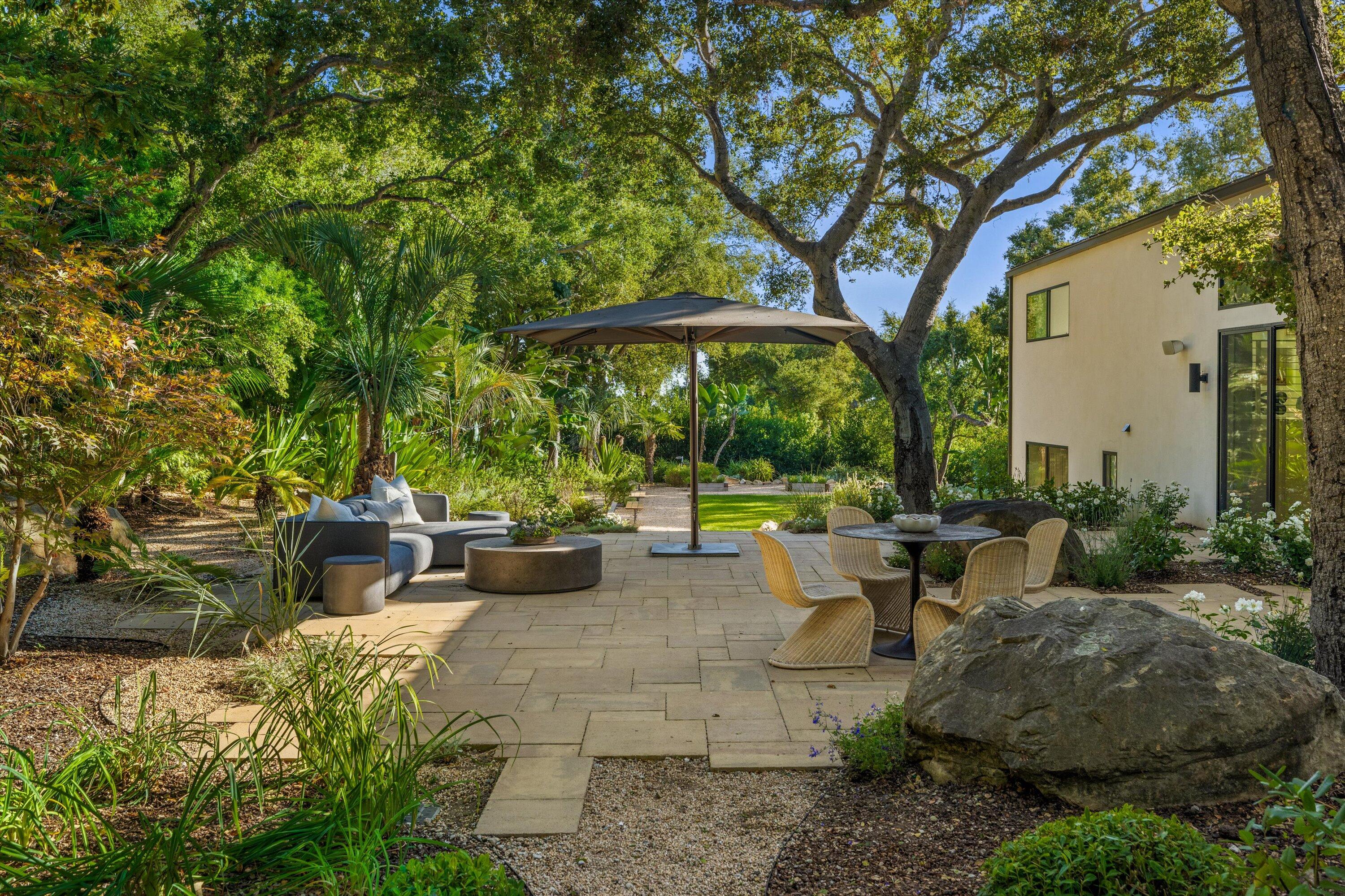 840 Riven Rock Road Montecito, CA 93108 - Photo 22 of 52 a view of a patio with couches and table and chairs under an umbrella with large trees
