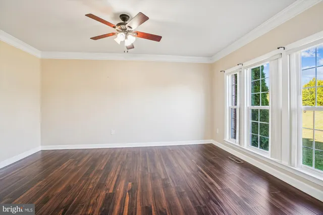 a view of an empty room with wooden floor and a ceiling fan