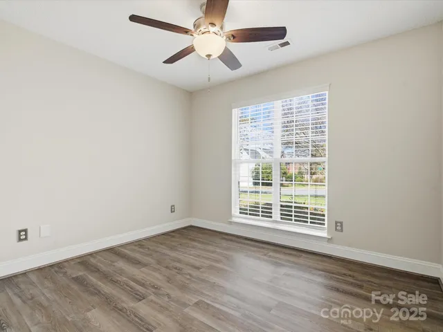 an empty room with wooden floor ceiling fan and windows
