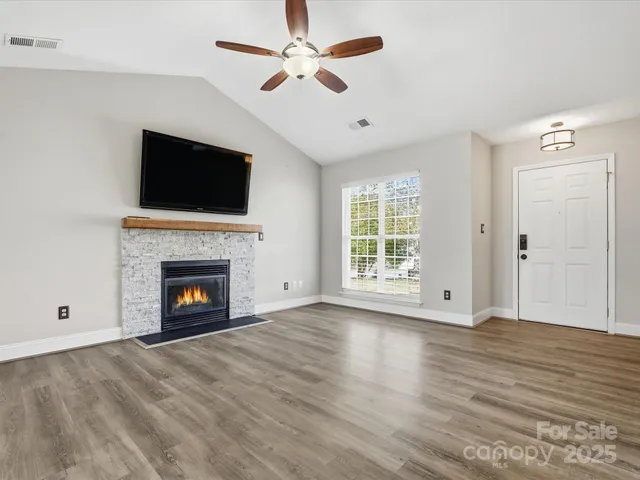 a view of an empty room with wooden floor fireplace and a window