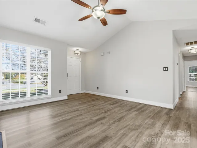 an empty room with wooden floor fan and windows