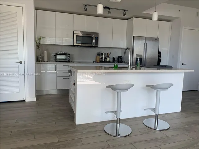 a kitchen with stainless steel appliances granite countertop a refrigerator a stove a sink and white cabinets with wooden floor